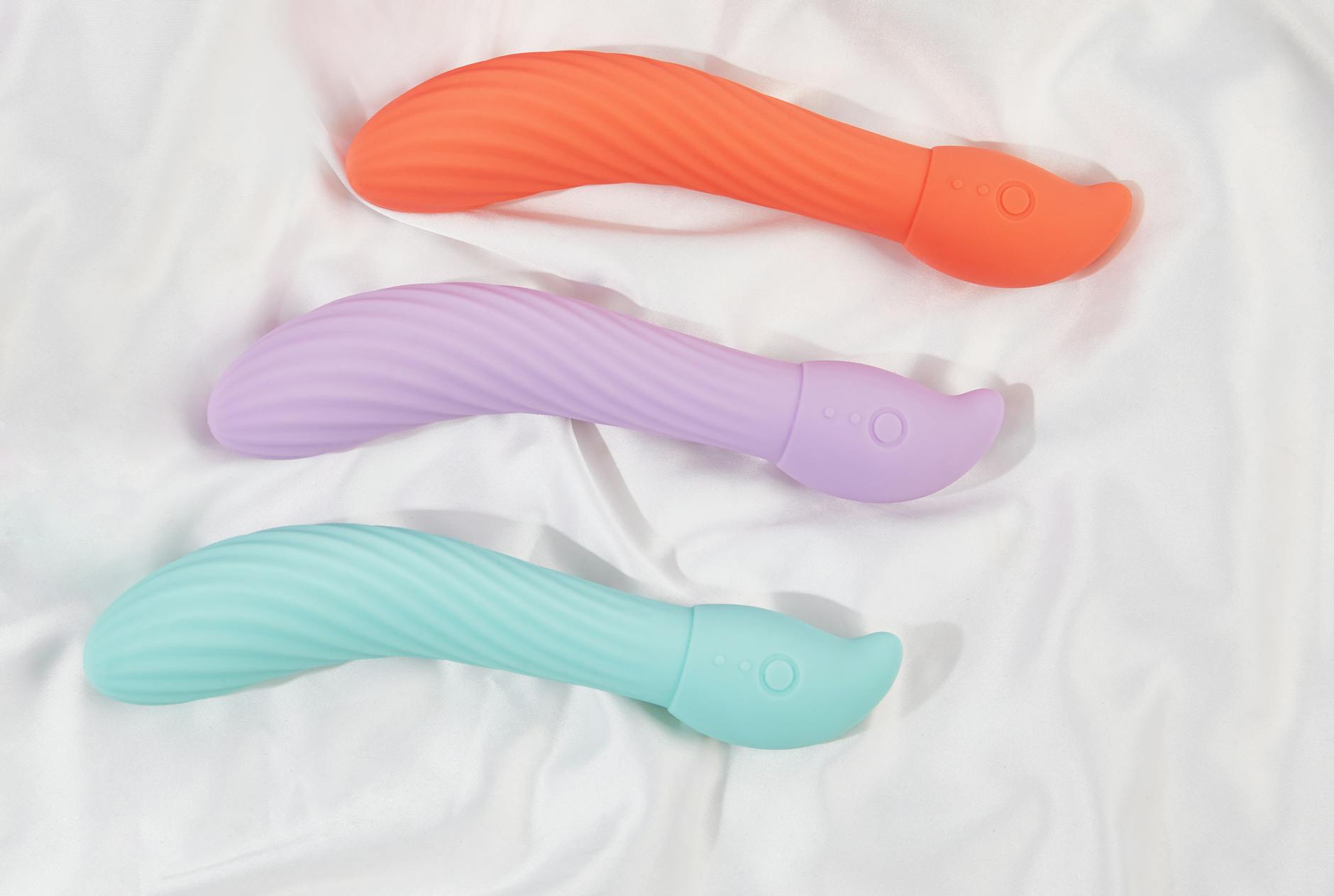 Three colorful vibrators arranged on white fabric, highlighting their smooth texture and modern design