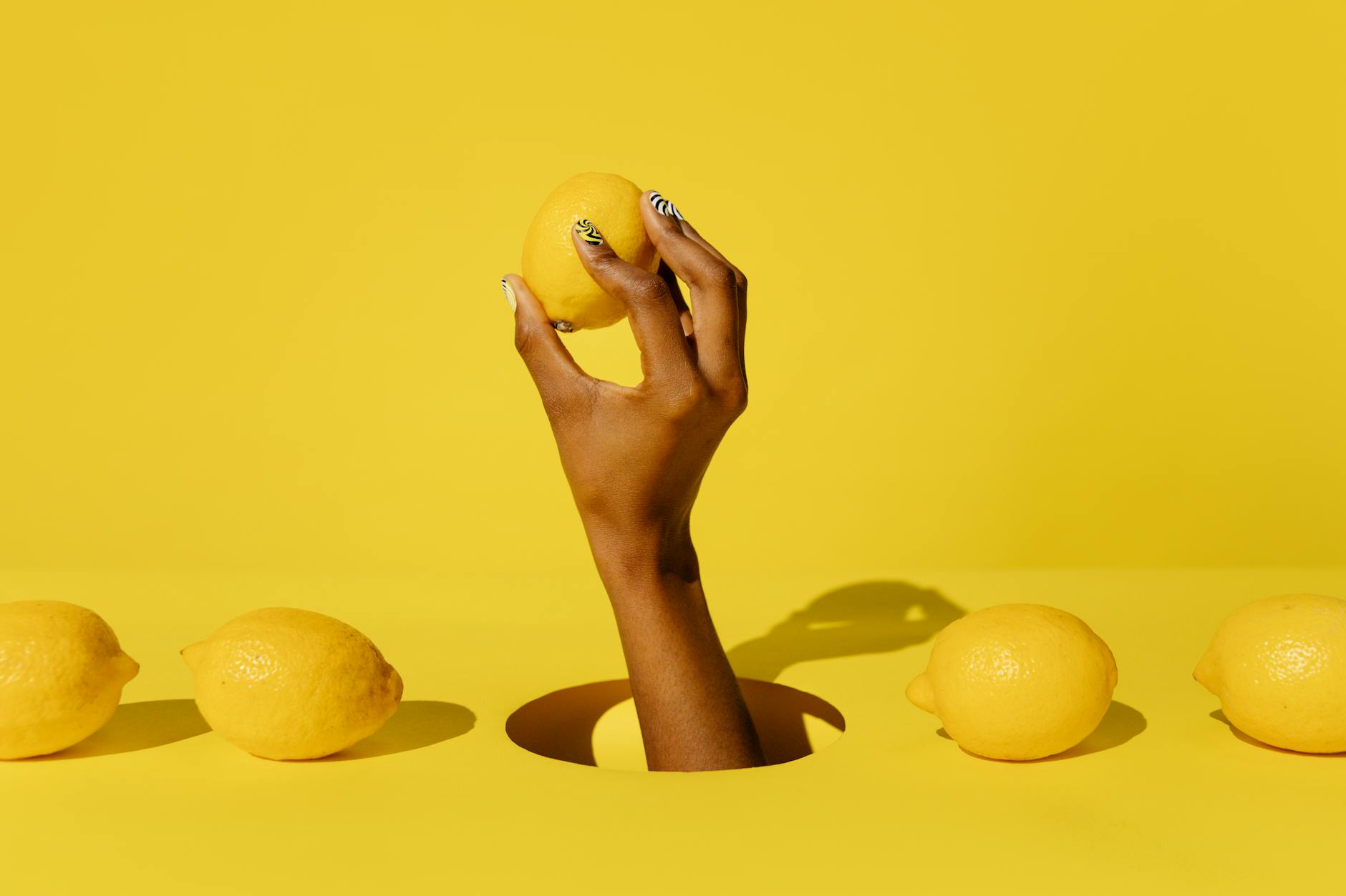 Hand holding a fresh lemon against yellow background, representing the lemon vibrator for extended arousal
