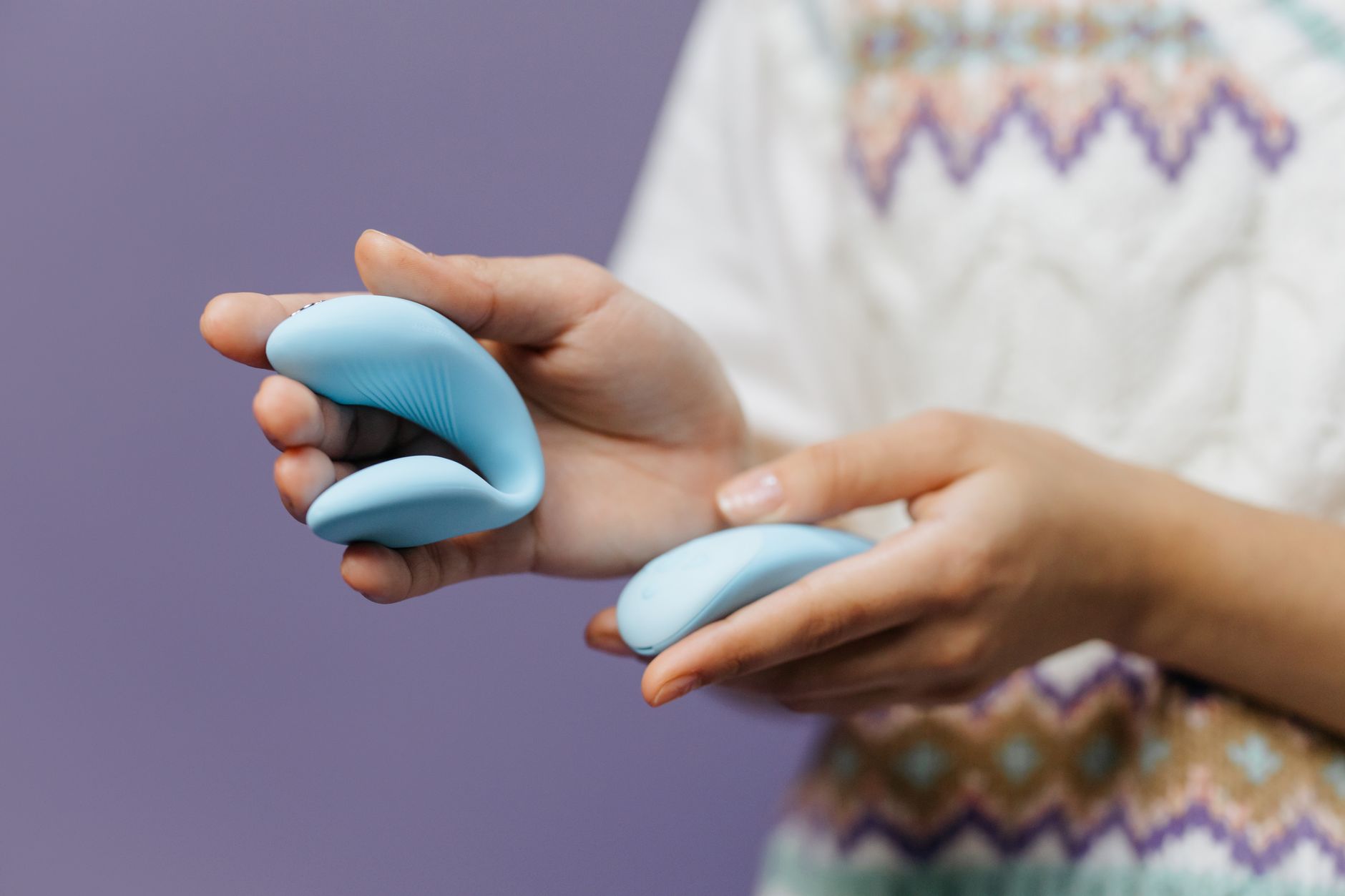 Close-up of hands holding a sleek lemon vibrator against a purple background, illustrating gentle control