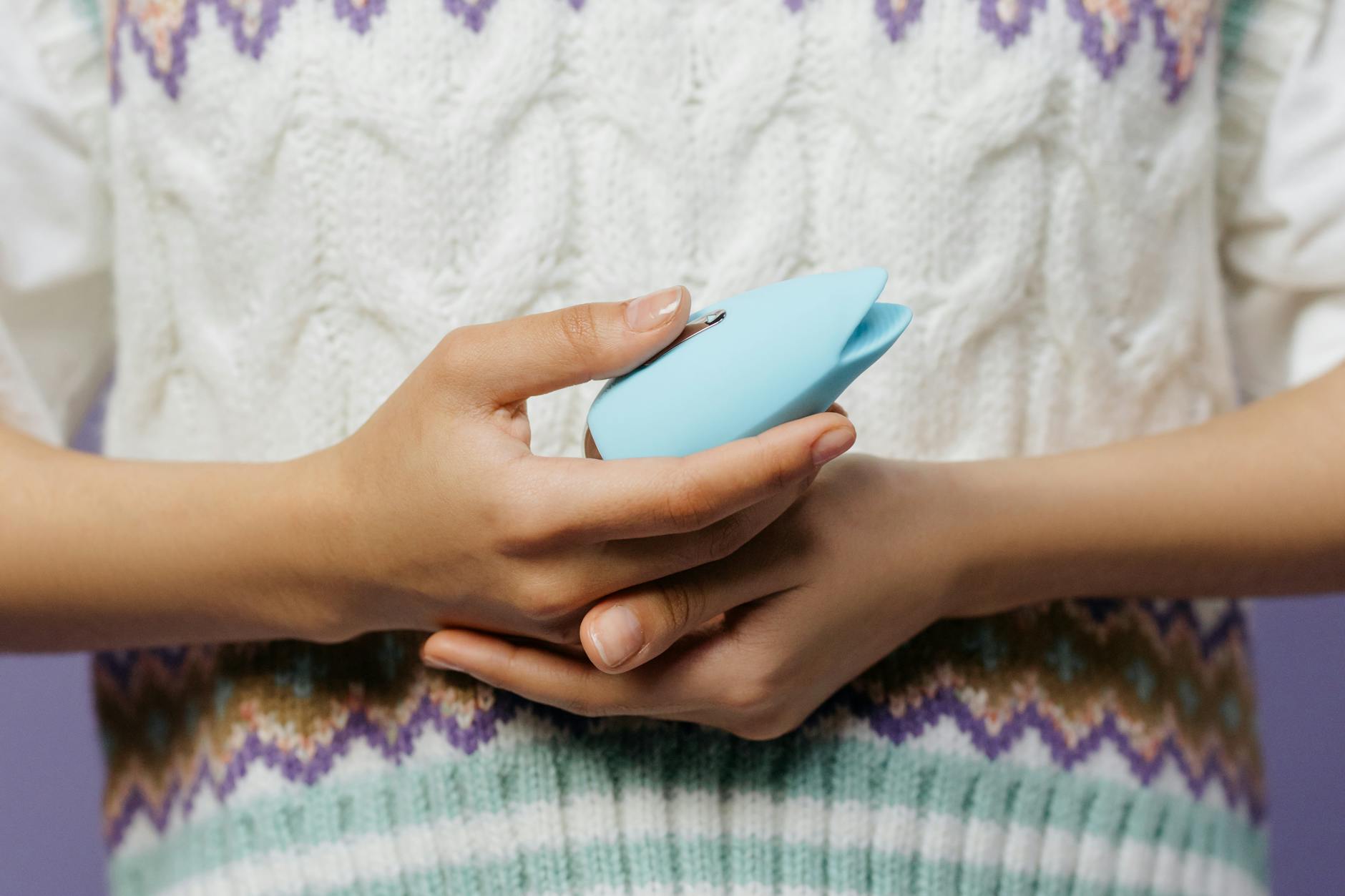 Mani che tengono un vibratore blu su un maglione lavorato a maglia, simbolo di intimità personale