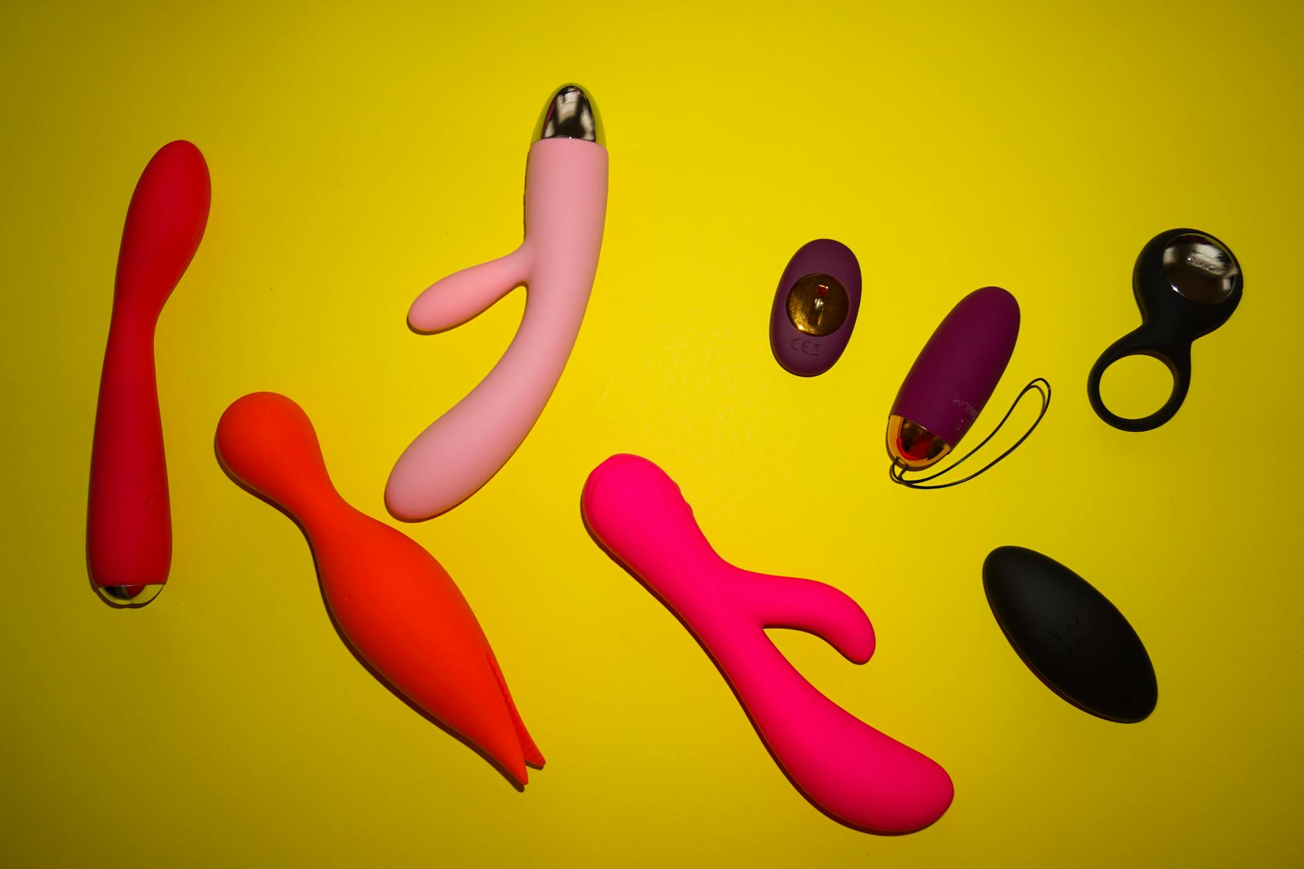 Vibrant collection of adult toys in various colors arranged on a bright yellow surface