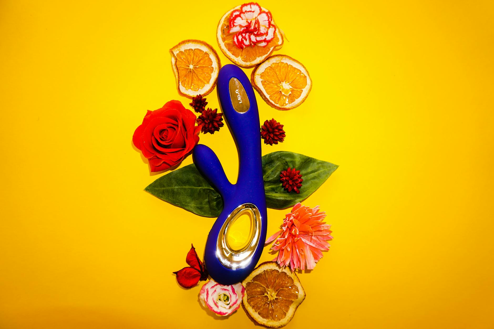 A blue lemon vibrator surrounded by flowers and fresh citrus on a bright yellow background